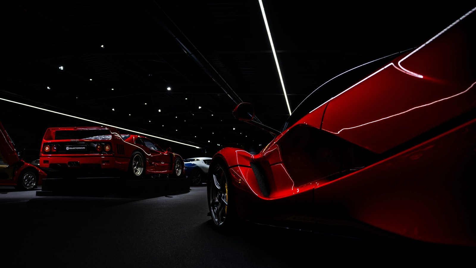 Striking red sports cars showcased in dramatic dim lighting at an indoor exhibition.